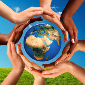 Conceptual peace and cultural diversity symbol of multiracial hands making a circle together around the world the Earth globe on blue sky and green grass background.